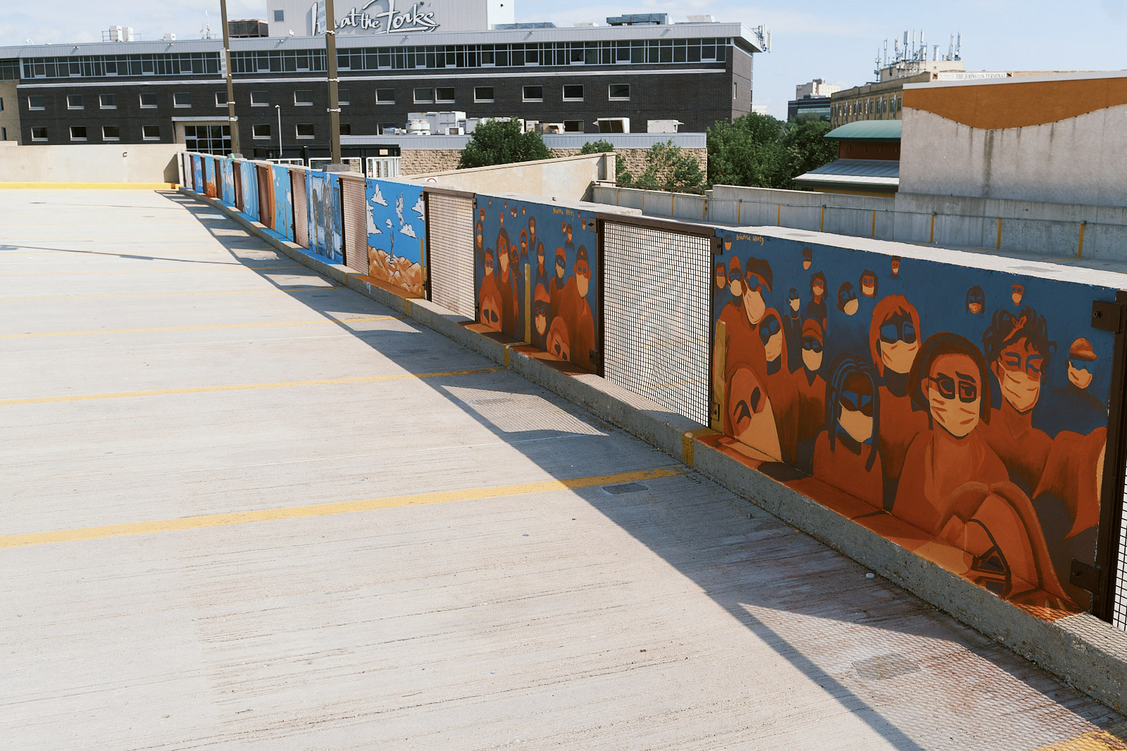 A photo of a roof top parking deck, with a series of half walls with murals painted on them. 